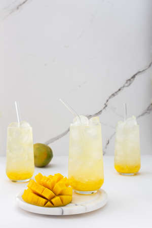 Refreshing drink with mango pulp in glasses with a glass straw on the background of a marble wall, cut mango next to the glassの写真素材