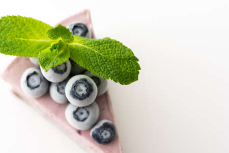 A piece of multi-colored delicious blueberry cheesecake decorated with mint and frozen blueberries close-up on a white backgroundの写真素材