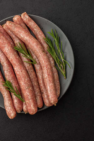 Raw pork sausages with rosemary in a plate close-up on a dark backgroundの写真素材
