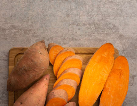 Whole and cut raw orange sweet potato on cutting board closeup, top viewの写真素材