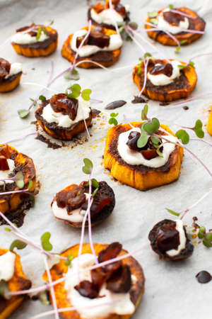 Oven baked sweet orange sweet potato wedges with yogurt and dates sprinkled with microgreens, sweet potato on parchment paper on a baking sheetの写真素材