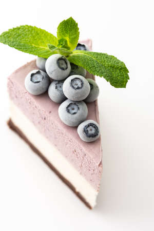 A piece of multi-colored delicious blueberry cheesecake decorated with mint and frozen blueberries close-up on a white backgroundの写真素材