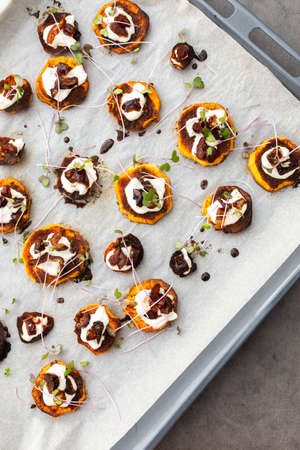 Oven baked sweet orange sweet potato wedges with yogurt and dates sprinkled with microgreens, sweet potato on parchment paper on a baking sheetの写真素材
