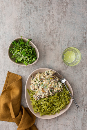 Green pasta from durum wheat and gravy with champignons fried in sour cream sauce with green onions and parsley and mozzarella, microgreens in a bowl and water with lemonの写真素材