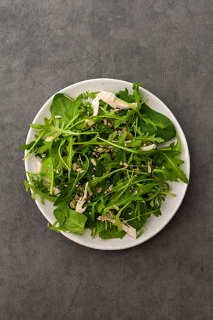 Delicious light salad with arugula and chicken breast sprinkled with various healthy seeds in a plate on a gray background, top viewの写真素材