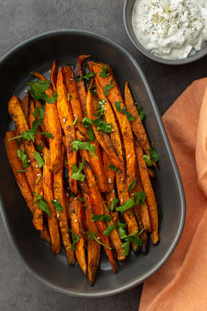 Oven baked orange sweet potato wedges with spices and oil in an oval ceramic dish, avocado sauce with yoghurt and spicesの写真素材