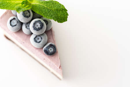 A piece of multi-colored delicious blueberry cheesecake decorated with mint and frozen blueberries close-up on a white backgroundの写真素材