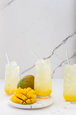 Refreshing drink with mango pulp in glasses with a glass straw on the background of a marble wall, cut mango next to the glassの写真素材