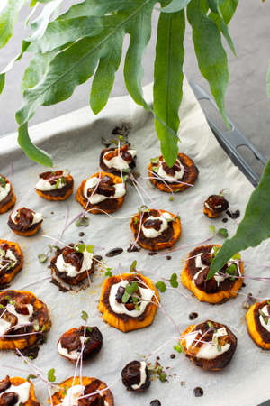 Oven baked sweet orange sweet potato wedges with yogurt and dates sprinkled with microgreens, sweet potato on parchment paper on a baking sheetの写真素材