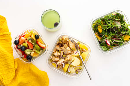 Home cooked food in lunch boxes for office, healthy eating at work and office food, new potatoes with chicken breast, salad and sliced fruits and berries, top viewの写真素材