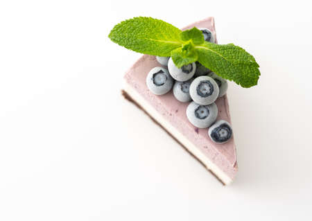A piece of multi-colored delicious blueberry cheesecake decorated with mint and frozen blueberries close-up on a white backgroundの写真素材
