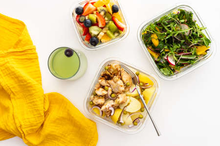 Home cooked food in lunch boxes for office, healthy eating at work and office food, new potatoes with chicken breast, salad and sliced fruits and berries, top viewの写真素材