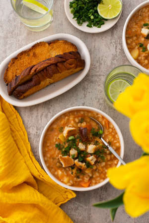 Soup with barley and sauerkraut, a plate with soup and croutons, top view on the table with food and a vase with tulips, delicious healthy lunch, Russian cuisineの写真素材