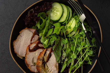 Hearty delicious lunch, fresh salad with cucumbers and microgreens of peas and with stewed pork, top view of the dark table with foodの写真素材