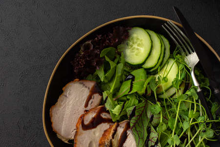 Hearty delicious lunch, fresh salad with cucumbers and microgreens of peas and with stewed pork, top view of the dark table with foodの写真素材