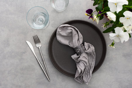 Table setting, empty plate with napkin and cutlery on the on the gray background, top view of the served table decorated with pansies flowersの写真素材
