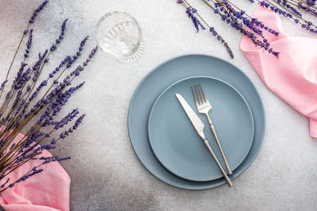 Table setting, empty plate with napkin and cutlery on a gray-pink concrete background, top view of the served table decorated with dry lavender flowersの写真素材
