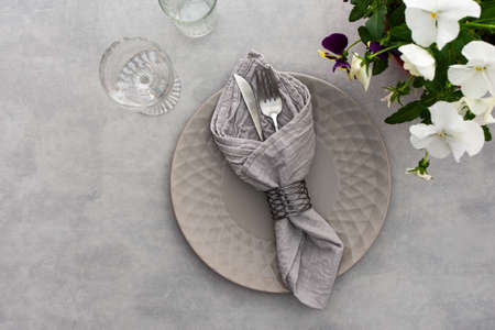 Table setting, empty plate with napkin and cutlery on the on the gray background, top view of the served table decorated with pansies flowersの写真素材