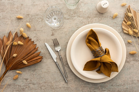 Table setting, plate with napkin and cutlery on a brown background, top view of the served table decorated with dry flowersの写真素材