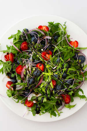 Light salad with arugula and berries, strawberries and blueberries, delicious healthy summer salad on a white backgroundの写真素材