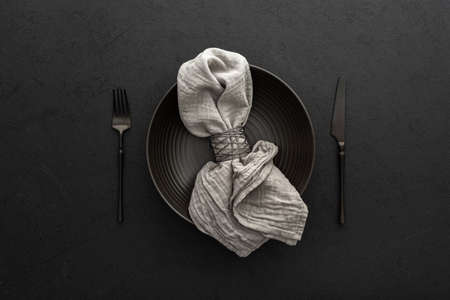 Table setting, empty plate with napkin and cutlery on a black background, top view of the served tableの写真素材
