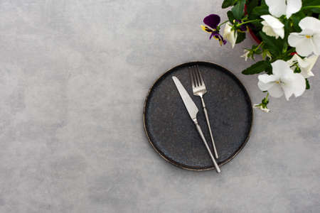 Table setting, empty plate and cutlery on the gray background, top view of the served table decorated with pansies flowersの写真素材