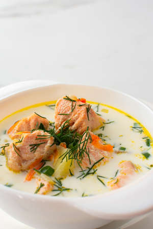 Norwegian red salmon fish soup with vegetables, herbs and cream, bowl of soup on a white marble backgroundの写真素材