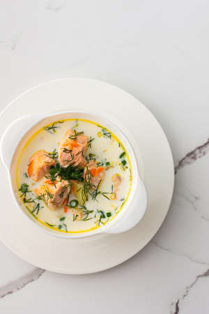 Norwegian red salmon fish soup with vegetables, herbs and cream, top view of a bowl of soup on a white marble backgroundの写真素材