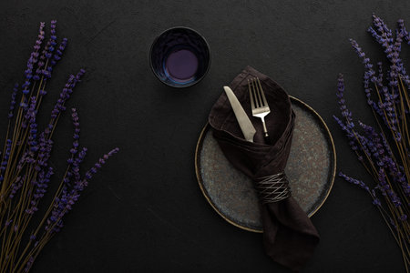 Table setting, empty plate with napkin and cutlery on a black background, top view of the served...