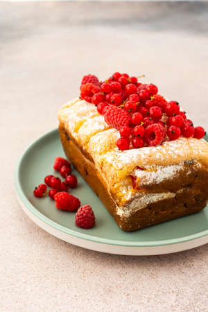 Rich sweet pie with fresh fruits, decorated with red currants and raspberries, in a plate on a pink backgroundの写真素材