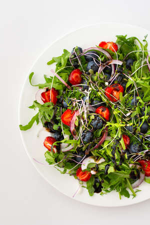 Light salad with arugula and berries, strawberries and blueberries, delicious healthy summer salad on a white backgroundの写真素材