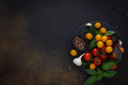 Food background, fresh ripe red and yellow tomatoes, spices and basil leaves, garlic and green onions on a dark board, healthy food concept, copy space, top viewの写真素材