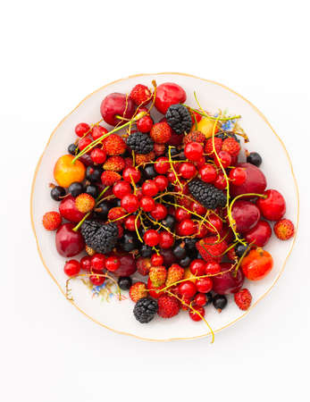 Fresh berries on a plate on a white background, red and black currants and black mulberries, wild strawberries and cherries, top viewの写真素材
