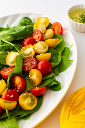 Salad with yellow and red tomatoes and spinach, top view of an oval plate with lettuce on a white backgroundの写真素材