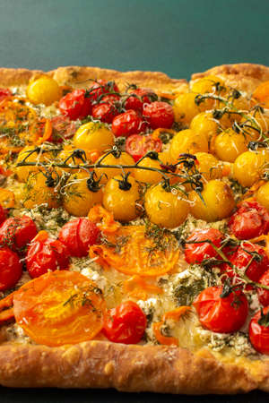 Homemade pie made of puff pastry and yellow, orange and red tomatoes, savory square pie on a green background, top view, copy spaceの写真素材