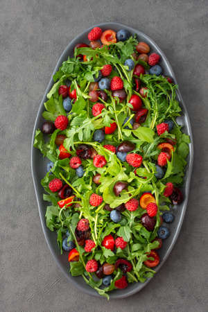 Delicious light salad of arugula and fresh sweet berries, black and red cherries and gooseberries, blueberries and raspberriesの写真素材