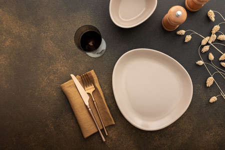 Table setting, empty plate with napkin and cutlery on a brown background, top view of the served table decorated with dry flowersの写真素材