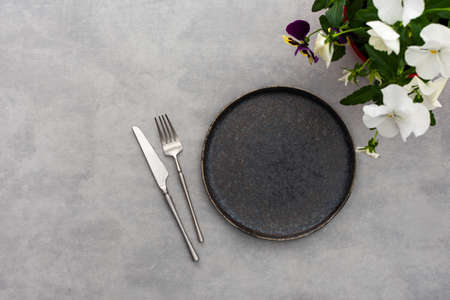 Table setting, empty plate and cutlery on the gray background, top view of the served table decorated with pansies flowersの写真素材