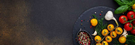 Food banner, fresh ripe red and yellow tomatoes, spices and basil leaves, garlic and green onions on dark board, healthy food concept, copy space, top viewの写真素材