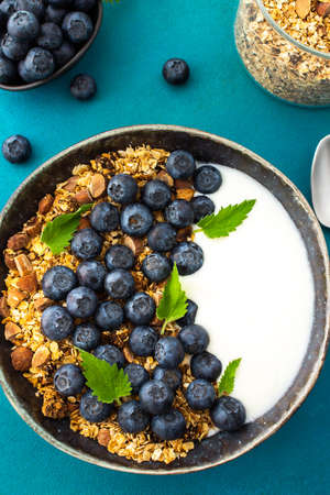Homemade granola with yogurt, blueberries and mint leaves in a bowl on a turquoise background, delicious healthy breakfastの写真素材