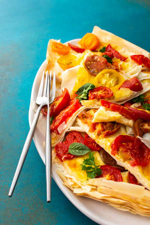 Pieces of puff pastry pie with colorful tomatoes with mozzarella, parsley and basil in an oval dishの写真素材