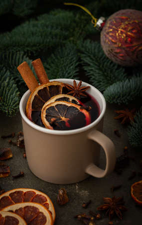 Christmas hot alcoholic drink mulled wine in a mug with citruses, aromatic spices and cinnamon among the spruce branchesの写真素材