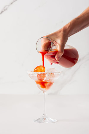 A man pours an alcoholic drink with tomato juice into a glass with ice