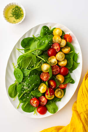 Salad with yellow and red tomatoes and spinach, top view of an oval plate with lettuce on a white backgroundの写真素材
