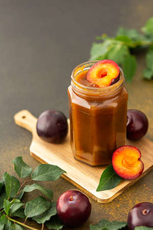 Homemade plum jam in a jar on a board with fresh plums, harvesting for the winterの写真素材