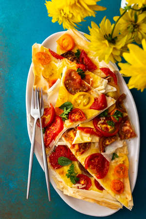 Pieces of puff pastry pie with colorful tomatoes with mozzarella, parsley and basil in an oval dishの写真素材