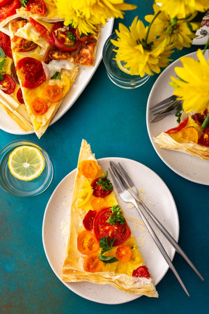 Portion of puff pastry pie with colorful tomatoes, parsley, basil and mozzarella in plates on the...