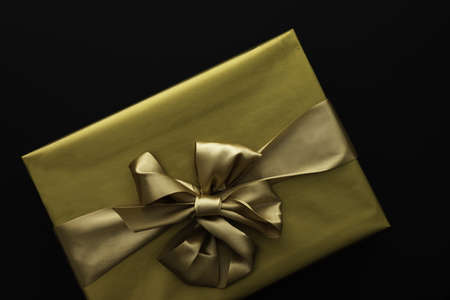 Gift box in a golden wrapper with a bow close-up on a black backgroundの写真素材