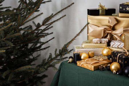 Preparations for the holiday, for dressing the Christmas tree, black and gold gifts and Christmas toys and decorations on the table near the fir treeの写真素材