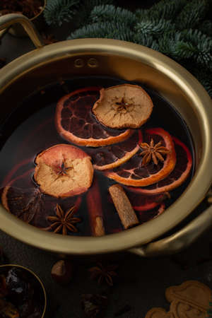 Christmas hot alcoholic drink mulled wine in a pan with citruses, aromatic spices, cinnamon and dried fruits among the spruce branchesの写真素材